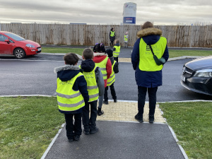 children in high visibility gear waiting to cross a road
